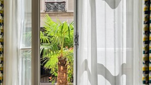 A room with a view of a balcony, a blue chair, and a potted plant. - La Maison Kléber – Luxury 1BR near Eiffel Tower & Champs-Élysées (Paris)