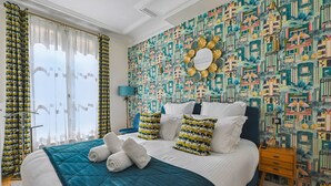 A hotel room with a large bed, a patterned wall, and a view of the city. - La Maison Kléber – Luxury 1BR near Eiffel Tower & Champs-Élysées (Paris)