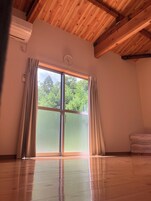 A room with a wooden ceiling, a large sliding glass door with curtains, a wall-mounted clock, and a stack of folded towels.