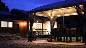 An outdoor covered patio with tables and chairs, a wooden building in the background, and a gravel ground. - Sasayakana Ouchi S Nogi (Futtsu)