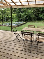 An outdoor wooden deck with tables and benches, surrounded by a garden with raised beds and a wooden fence.