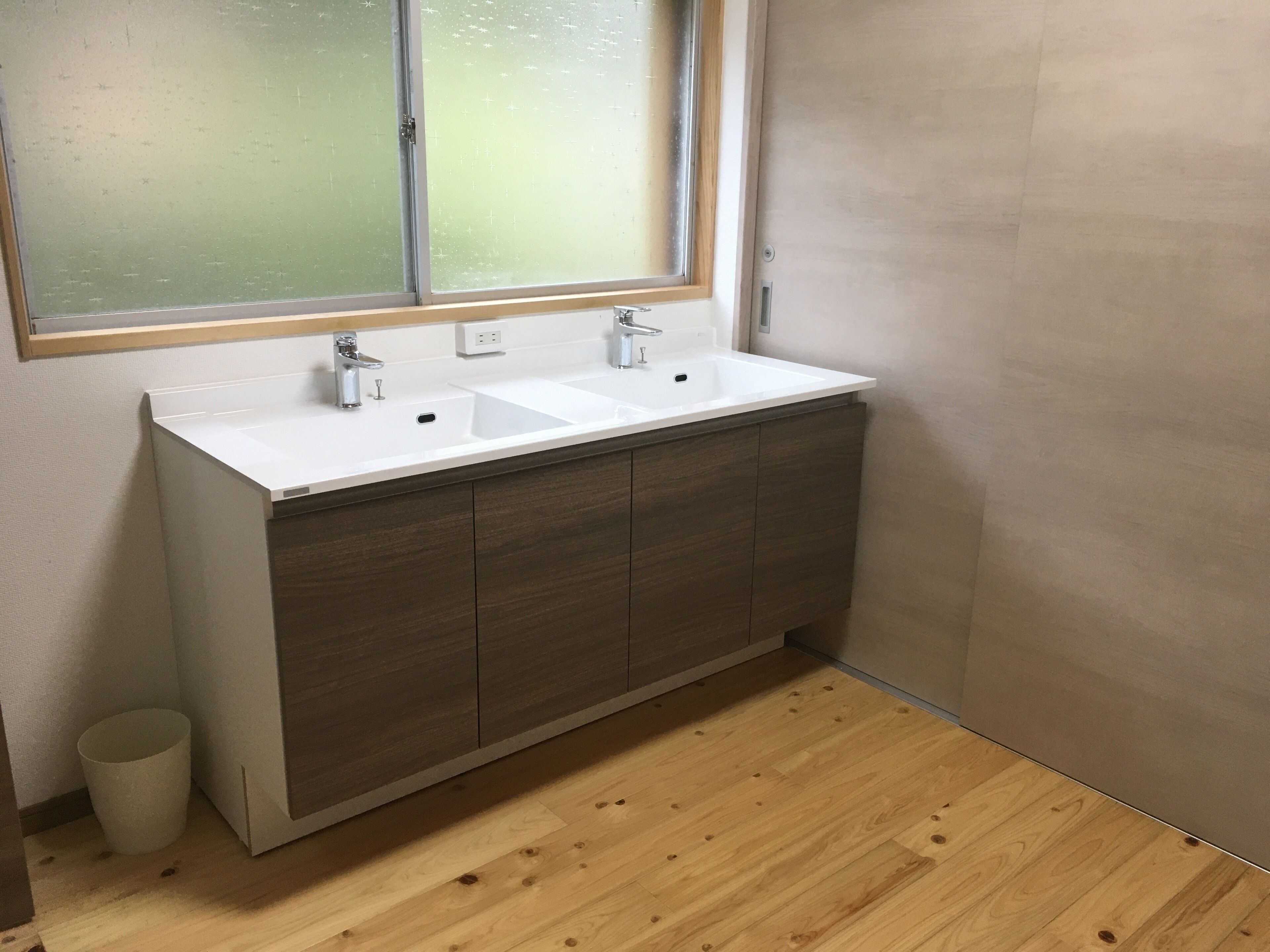 A bathroom with a white sink, wooden cabinets, and a window above the sink.