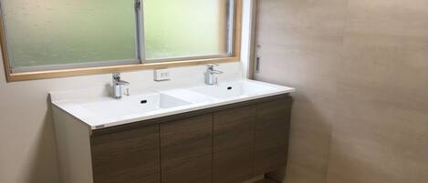 A bathroom with a white sink, wooden cabinets, and a window above the sink.