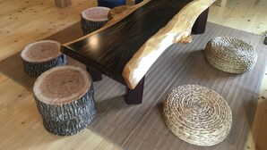 A wooden bench with a natural finish, surrounded by round stools and woven ottomans on a wooden floor. - Sasayakana Ouchi S Nogi (Futtsu)