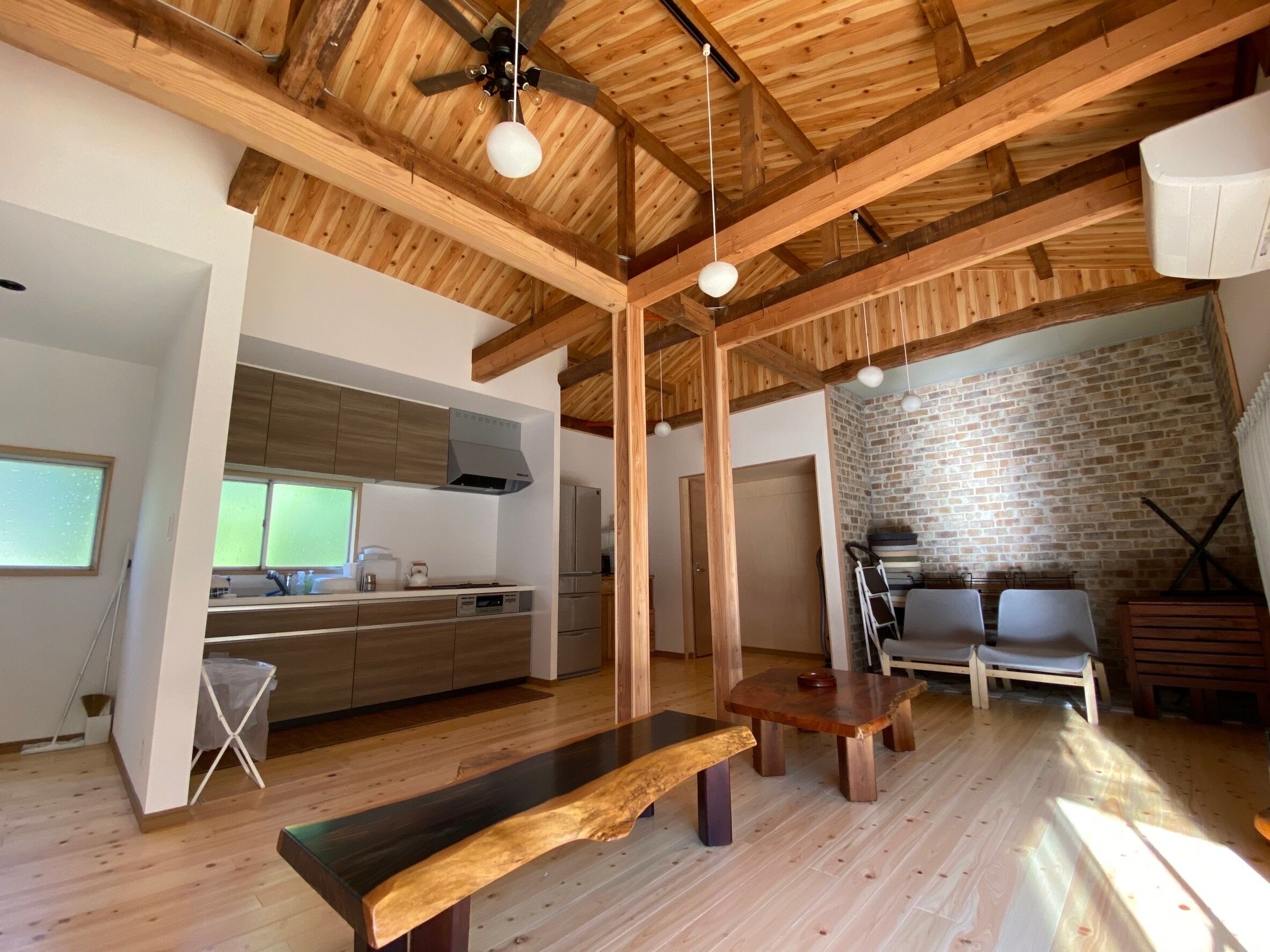 A spacious living area with a wooden ceiling, a built-in kitchen, and a brick wall.