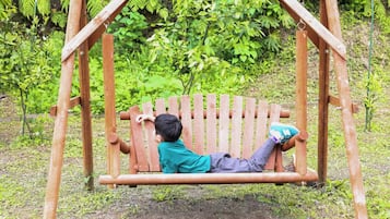 A wooden swing set in a garden with lush greenery in the background.