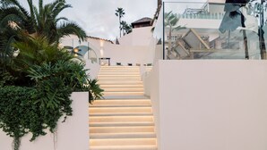 Un escalier avec un mur blanc d’un côté et une rambarde en verre de l’autre, menant à un niveau supérieur.