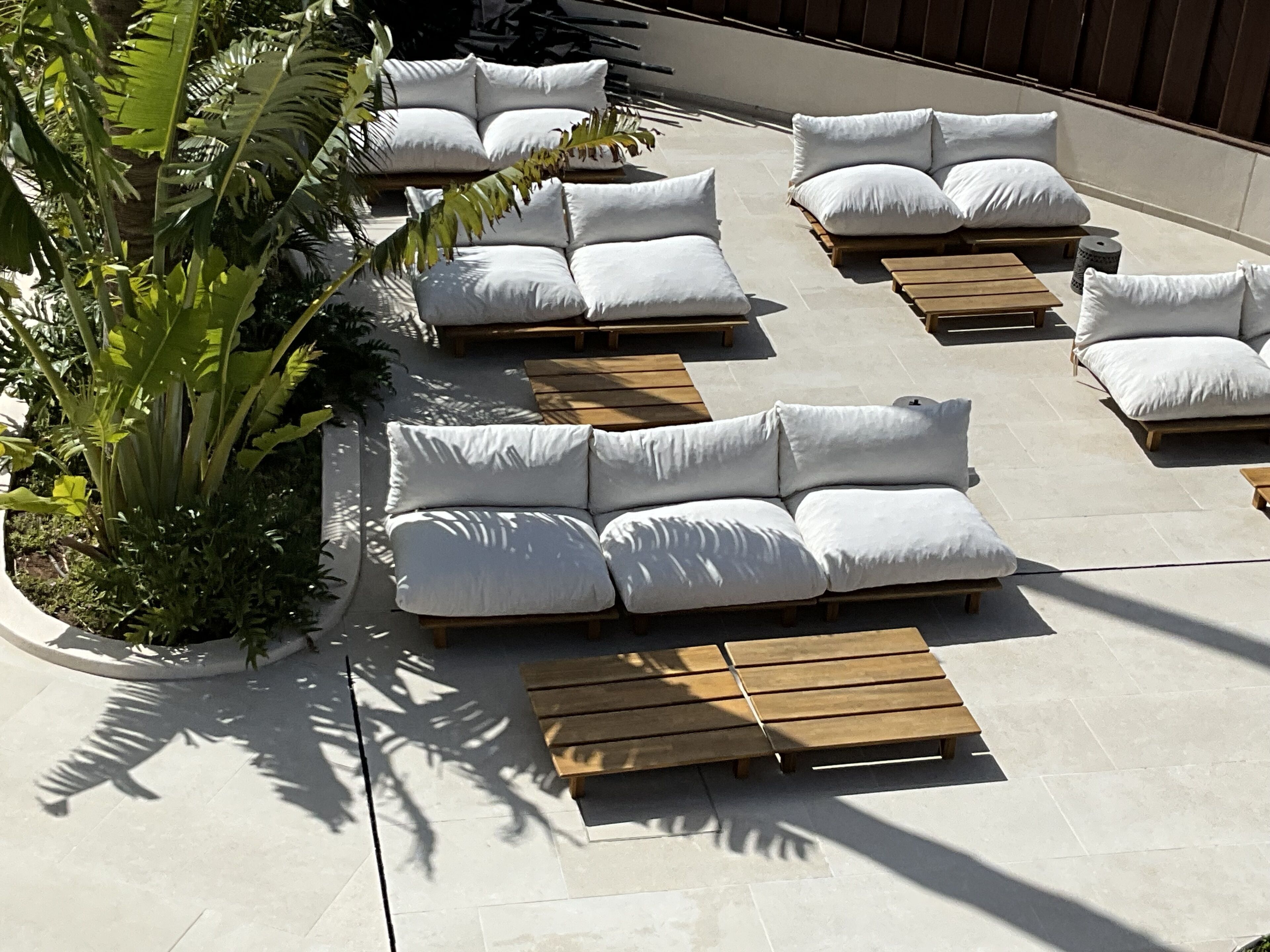 Outdoor seating with white cushions and wooden tables, surrounded by potted plants.