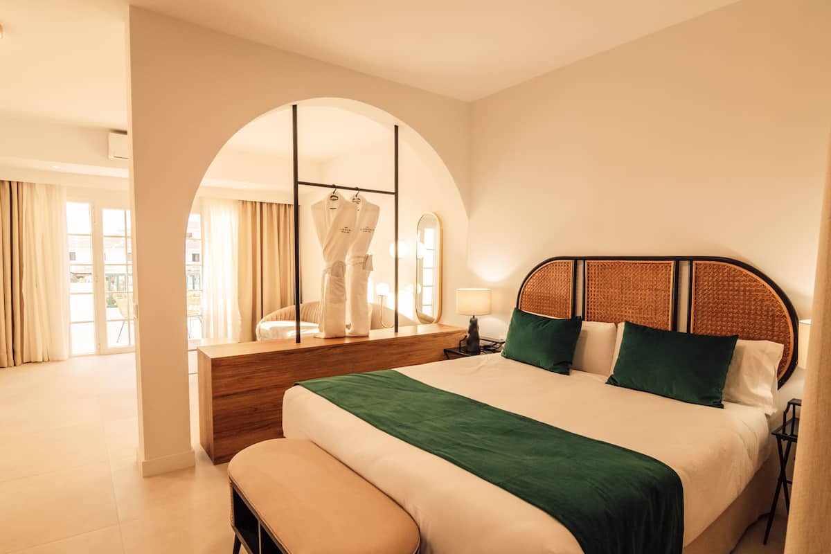 Een hotelkamer met een groot bed, een houten nachtkastje, een bankje en een spiegel.