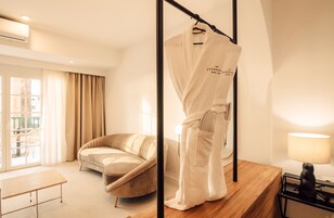 Quarto de hotel moderno com sofá, roupão pendurado, mesa de madeira e luminária.