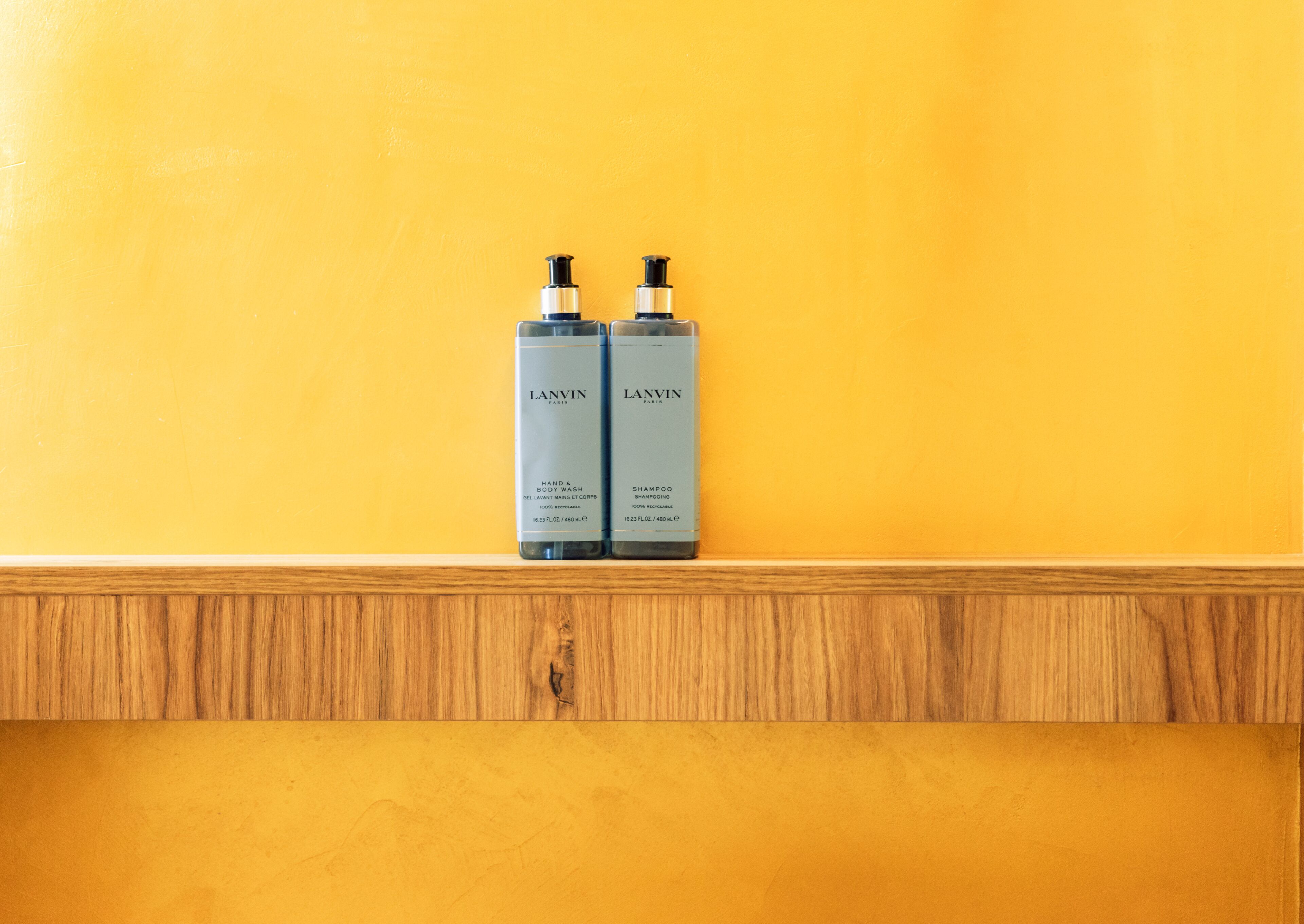 Two Lanvin shampoo bottles on a wooden shelf against a yellow wall.