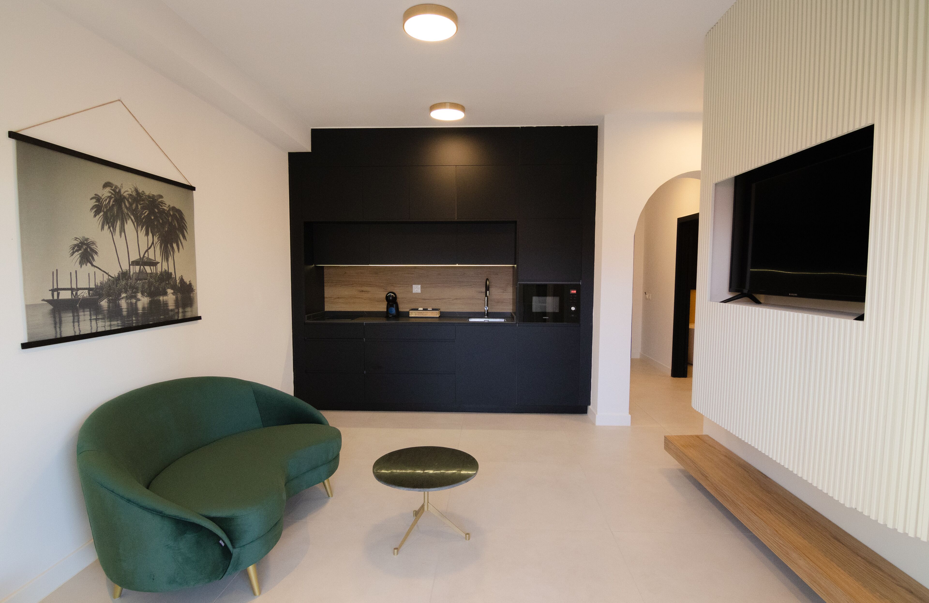 Een moderne woonkamer met een groene bank, een klein rond tafeltje en een keukenhoek met een zwart aanrecht en een houten achterwand.