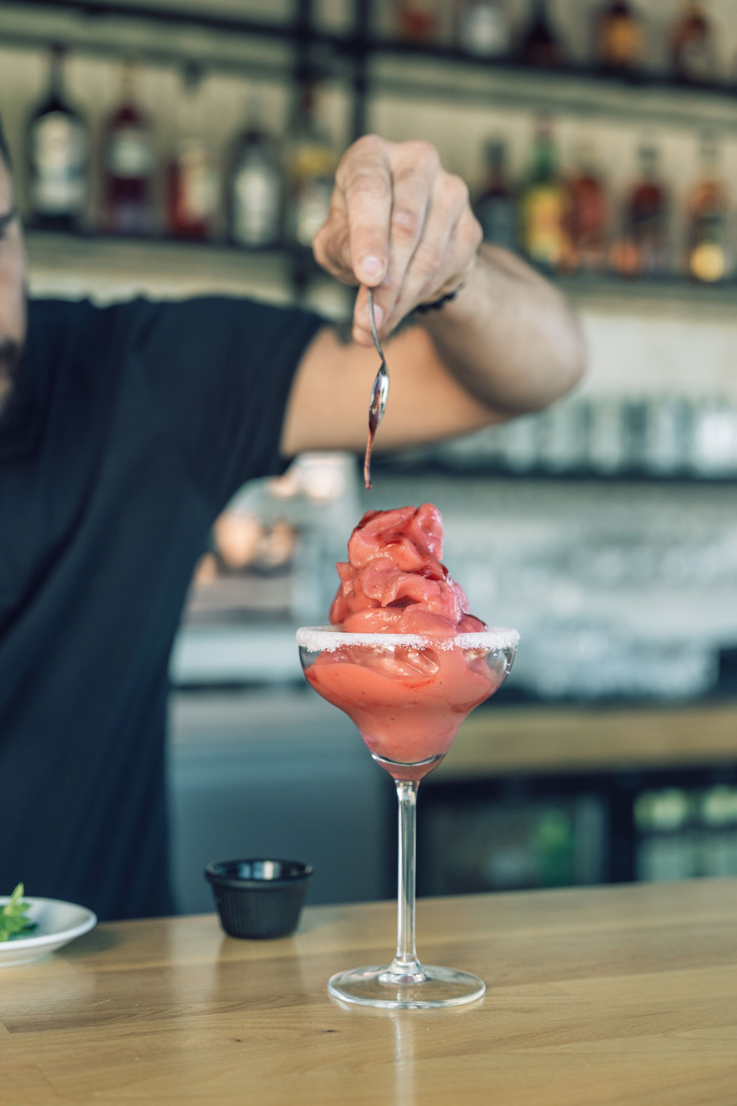 Una persona vertiendo una bebida rosa en un vaso con borde salado.