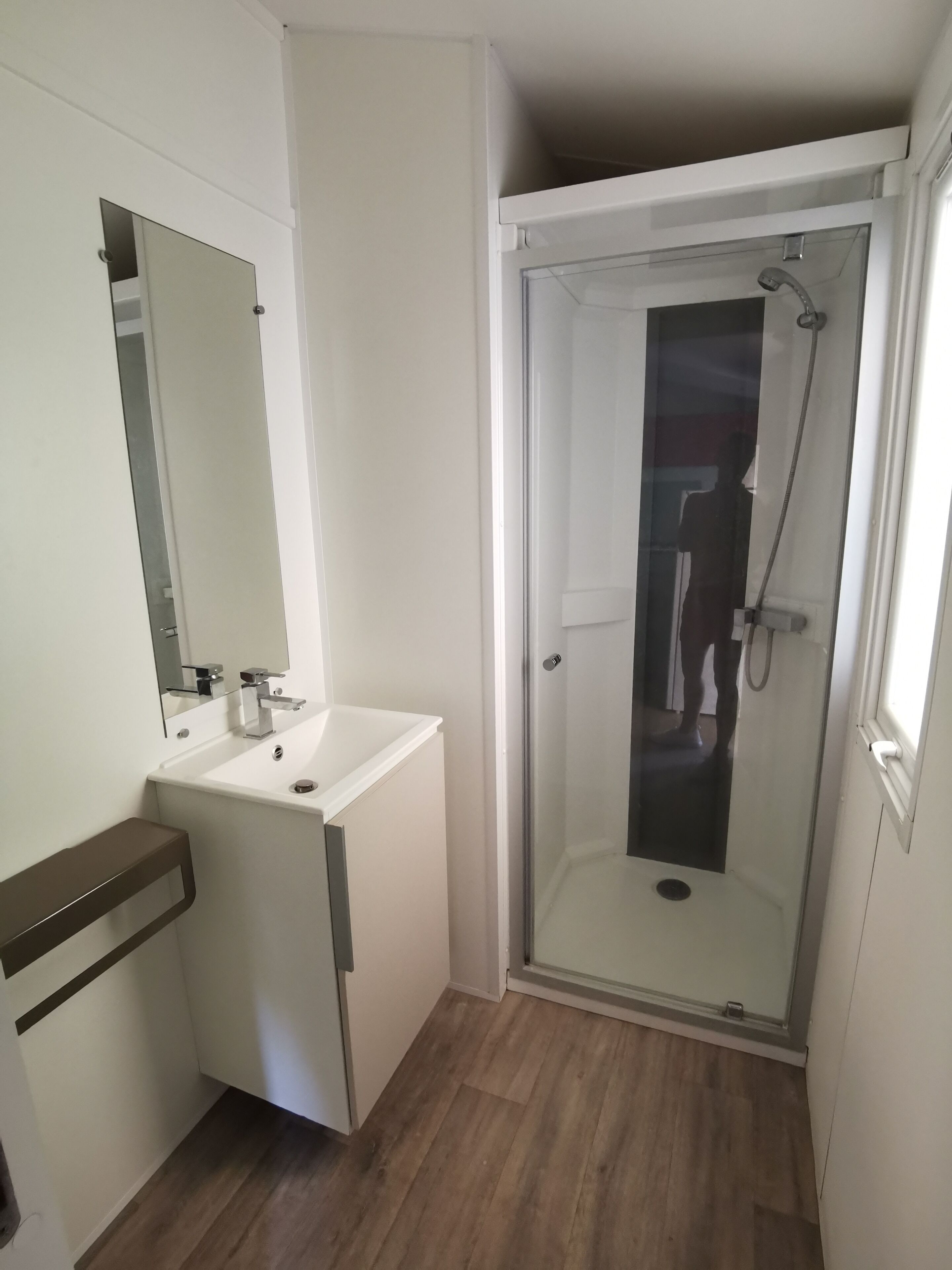 A modern bathroom with a glass-enclosed shower, a white sink with a mirror, and a wooden floor.