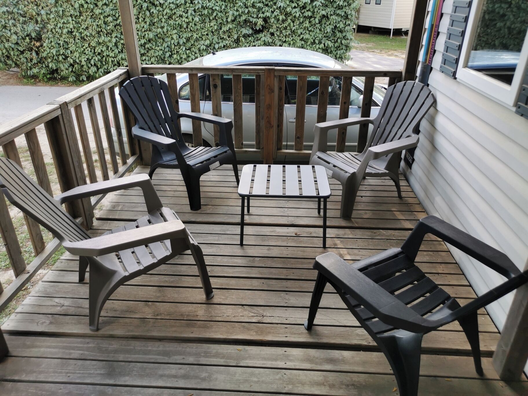 Una terraza de madera con cuatro sillas Adirondack y una mesita, rodeada por una barandilla de madera.