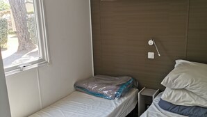 A small, single-bed room with a window, a bedside table, and a headboard with shelves.
