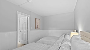 Une chambre avec deux lits, une table de chevet avec une lampe, une porte et un tableau encadré au mur.