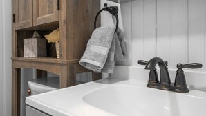 Ein Badezimmer mit einem weißen Waschbecken, einem schwarzen Wasserhahn und einem Holzboden mit einem Handtuch.