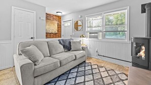 Un salon moderne avec un canapé gris, un tapis à motifs, une cheminée et de grandes fenêtres équipées de stores.