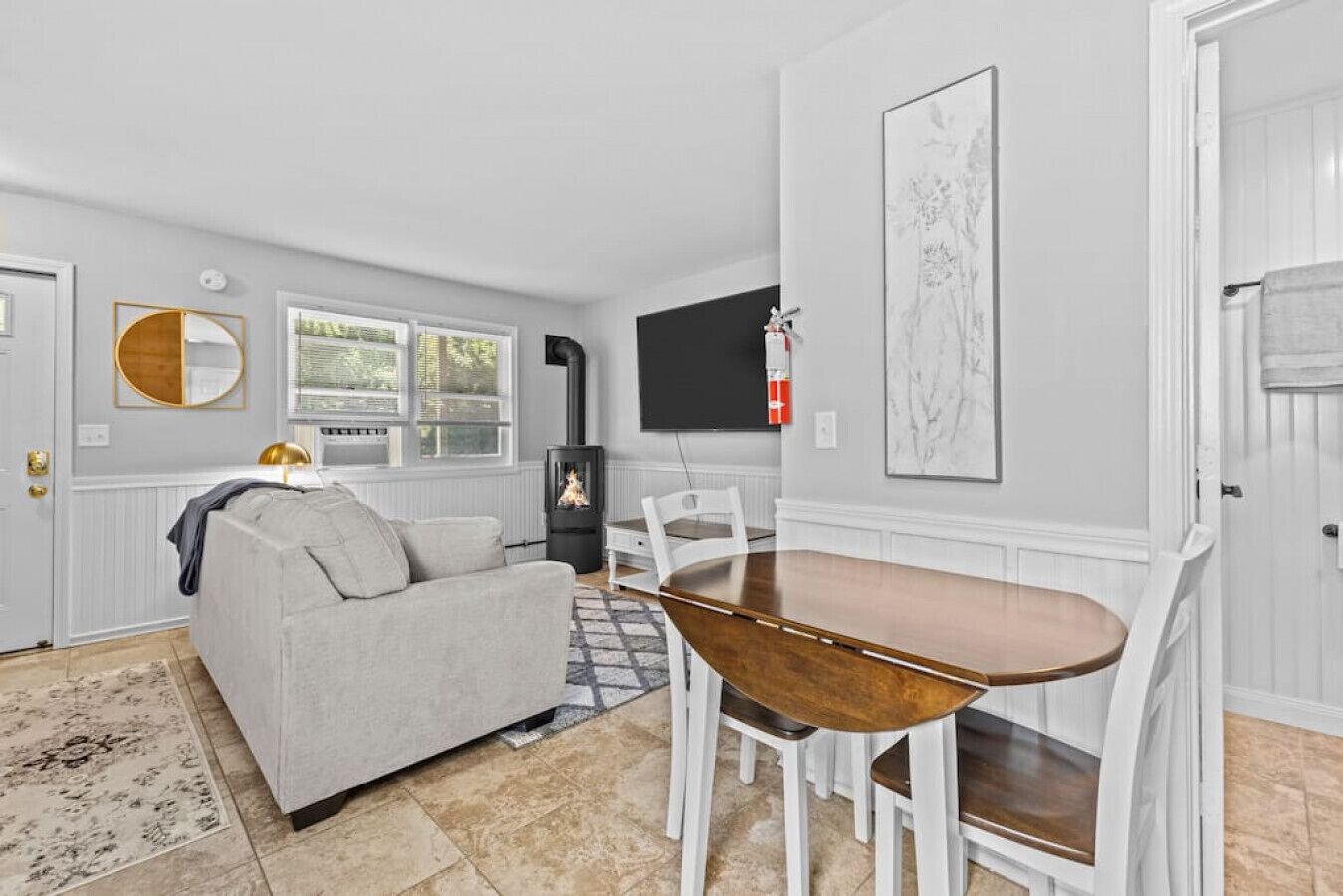 Un salon moderne comprenant un canapé, une table à manger avec des chaises, une cheminée et un téléviseur fixé au mur.