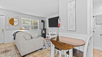 A modern living room with a sofa, a dining table with chairs, a fireplace, and a TV mounted on the wall.