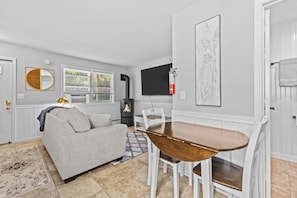A modern living room with a sofa, a dining table with chairs, a fireplace, and a TV mounted on the wall.