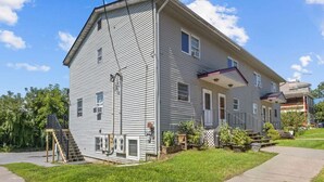 Une maison à deux étages avec un porche à l’avant, un petit jardin et un escalier bien visible menant à l’entrée.