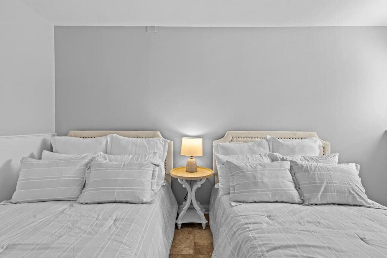 A bedroom with two beds, a bedside table with a lamp, and a neutral color scheme.