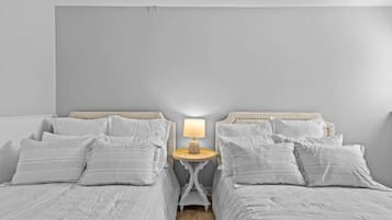 A bedroom with two beds, a bedside table with a lamp, and a neutral color scheme.