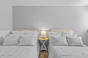 A bedroom with two beds, a bedside table with a lamp, and a neutral color scheme.