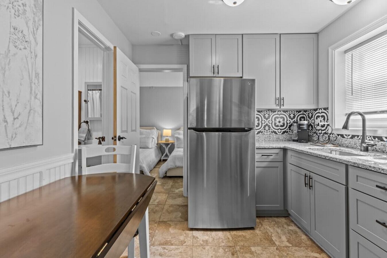 A modern kitchen with a stainless steel refrigerator, grey cabinets, and a wooden dining table.