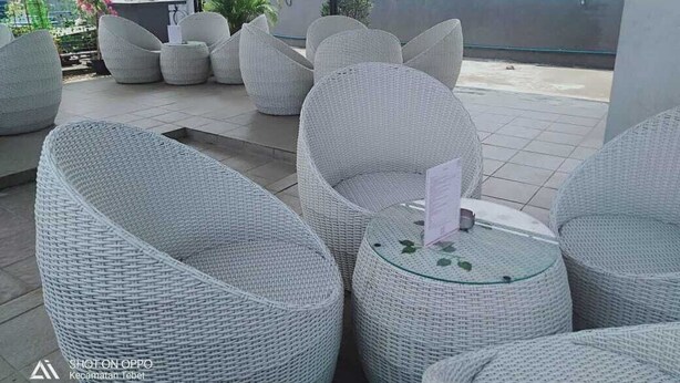 A rooftop terrace with wicker furniture and a small table with a menu. - DAIMA Syariah Mansion Tebet (Jakarta)