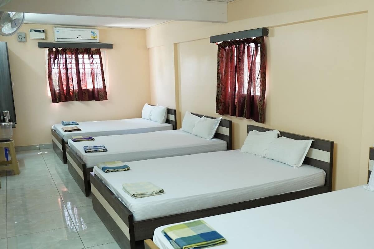 A hotel room with four single beds, a ceiling fan, an air conditioning unit, and a window with curtains.