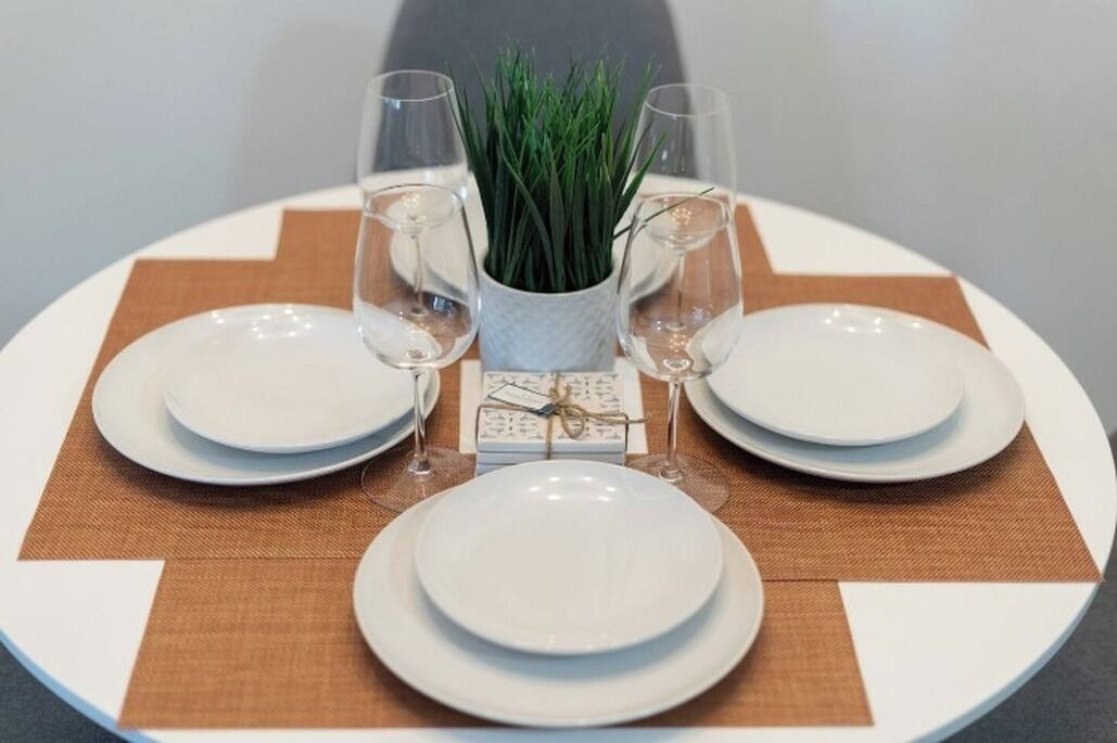 A round table set with white plates, two wine glasses, and a small potted plant.