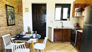 A compact kitchen with a dining area, featuring a tiled floor, wooden cabinets, a black refrigerator, and a white sink. - Cute Apple - At The Heart Of The Old Town (Chania)