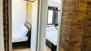 A small, compact room with two single beds, a brick wall, and a window. - Cute Apple - At The Heart Of The Old Town (Chania)