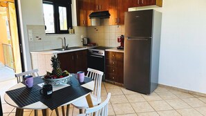 A kitchen with wooden cabinets, a stainless steel refrigerator, a dining table with chairs, and a window above the sink. - Cute Apple - At The Heart Of The Old Town (Chania)