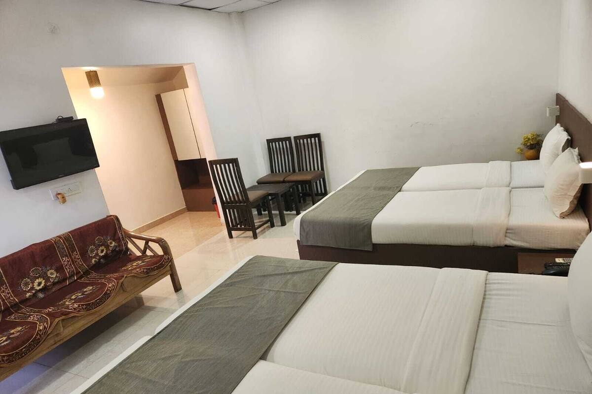 A hotel room with two beds, a sofa, a TV, and a dining area.
