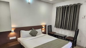 Une chambre d’hôtel avec un grand lit, des tables de chevet, un bureau et une fenêtre avec des rideaux.