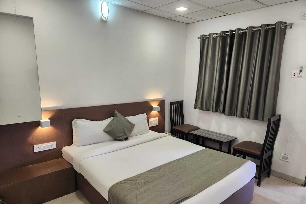 A hotel room with a large bed, bedside tables, a desk, and a window with curtains.
