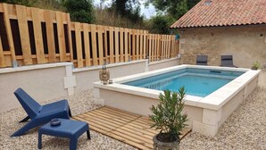 Una piscina con muelle de madera, dos sillas de descanso y una planta en maceta.