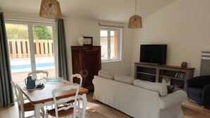 Una sala de estar con un sofá, un televisor, un mueble de madera y una mesa de comedor con sillas.