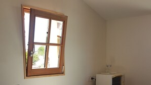 A small dining area with a table, chairs, a microwave, and a window. - Joli Petit Appartement Neuf, au Calme et à Proximité de la mer et des Commerces (La Guérinière)