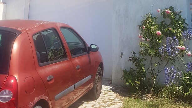 A white building with a tiled roof, a garage door, and a red car parked in front. - Joli Petit Appartement Neuf, au Calme et à Proximité de la mer et des Commerces (La Guérinière)