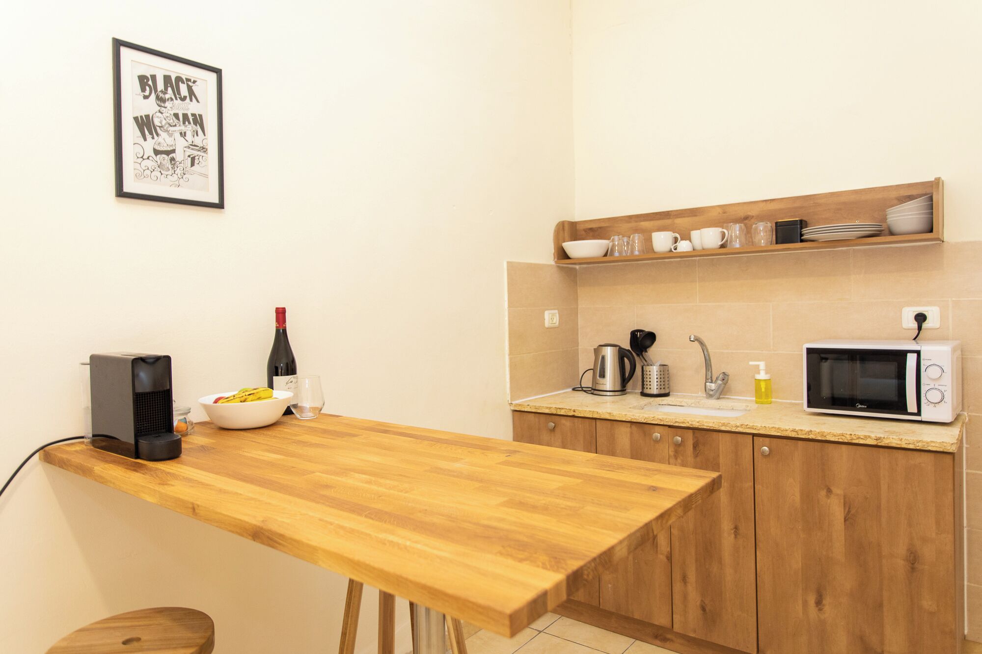 Eine Küche mit Holzschränken, einer Mikrowelle, einem Wasserkocher, einer Weinflasche und einem gerahmten Bild an der Wand.