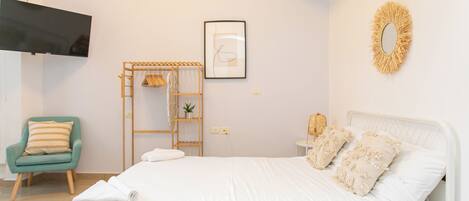 A bedroom with a bed, a chair, a TV, a shelf, and a wall decoration.