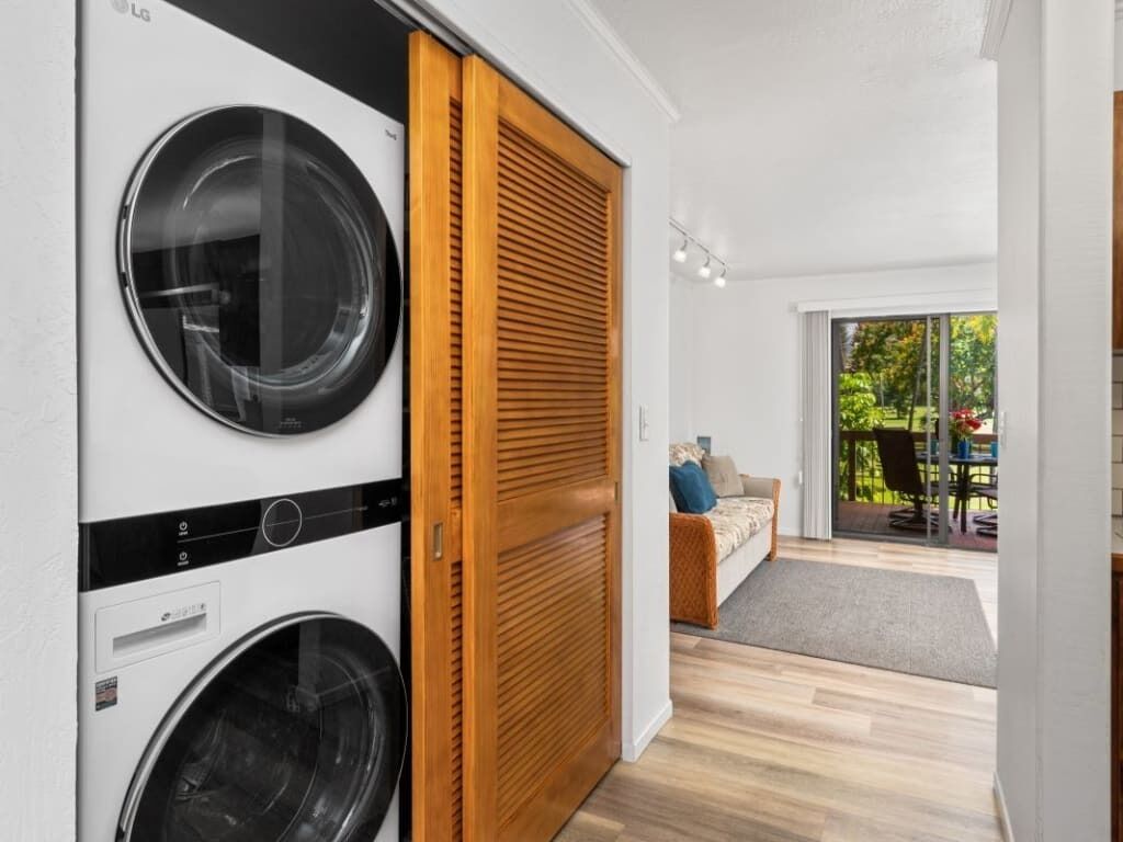 A laundry room with two washing machines, a wooden door, and a view of an outdoor patio with a sofa and table.
