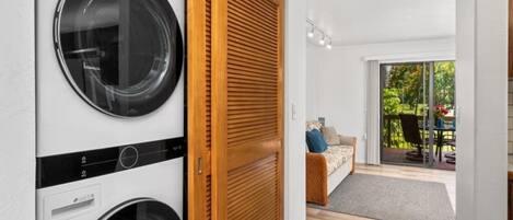 A laundry room with two washing machines, a wooden door, and a view of an outdoor patio with a sofa and table.