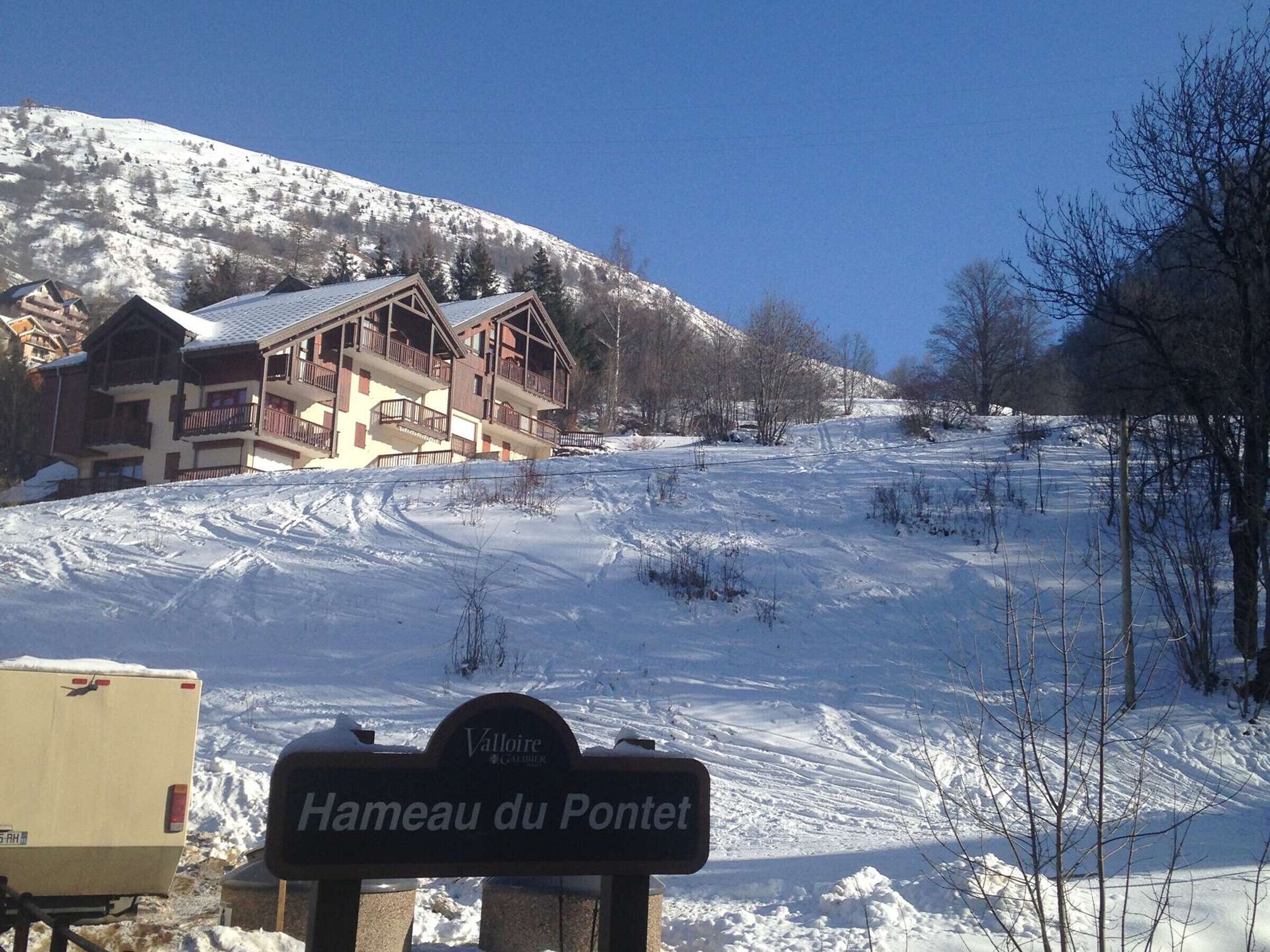 A sign for "Hameau du Pontet" with a snow-covered landscape and a building in the background.