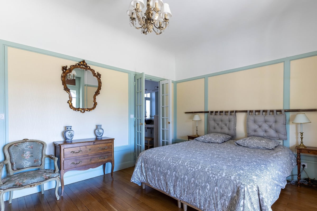 Un dormitorio con una cama grande, un aparador, una silla, un espejo y una araña.